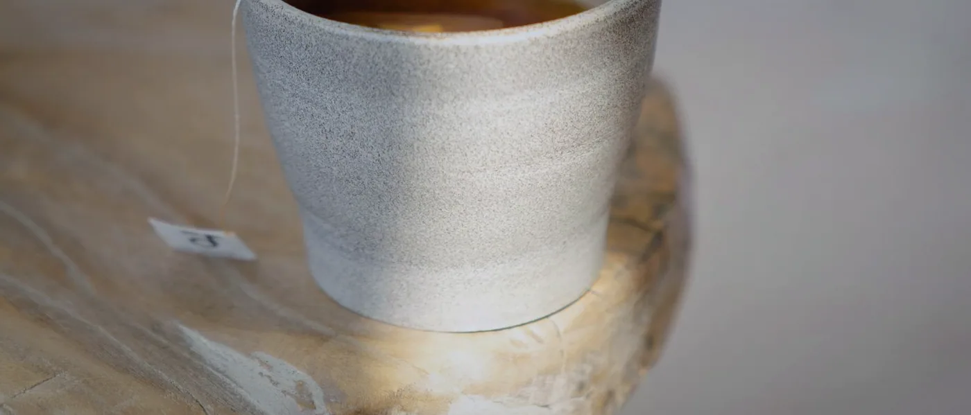 A stoneware cup of tea, the tag of the bag still hanging over the rim